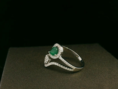 18k gold bypass ring with 0.59 ct pear-cut emerald, pear-shaped diamond cluster, and pavé diamonds, modern asymmetrical design.