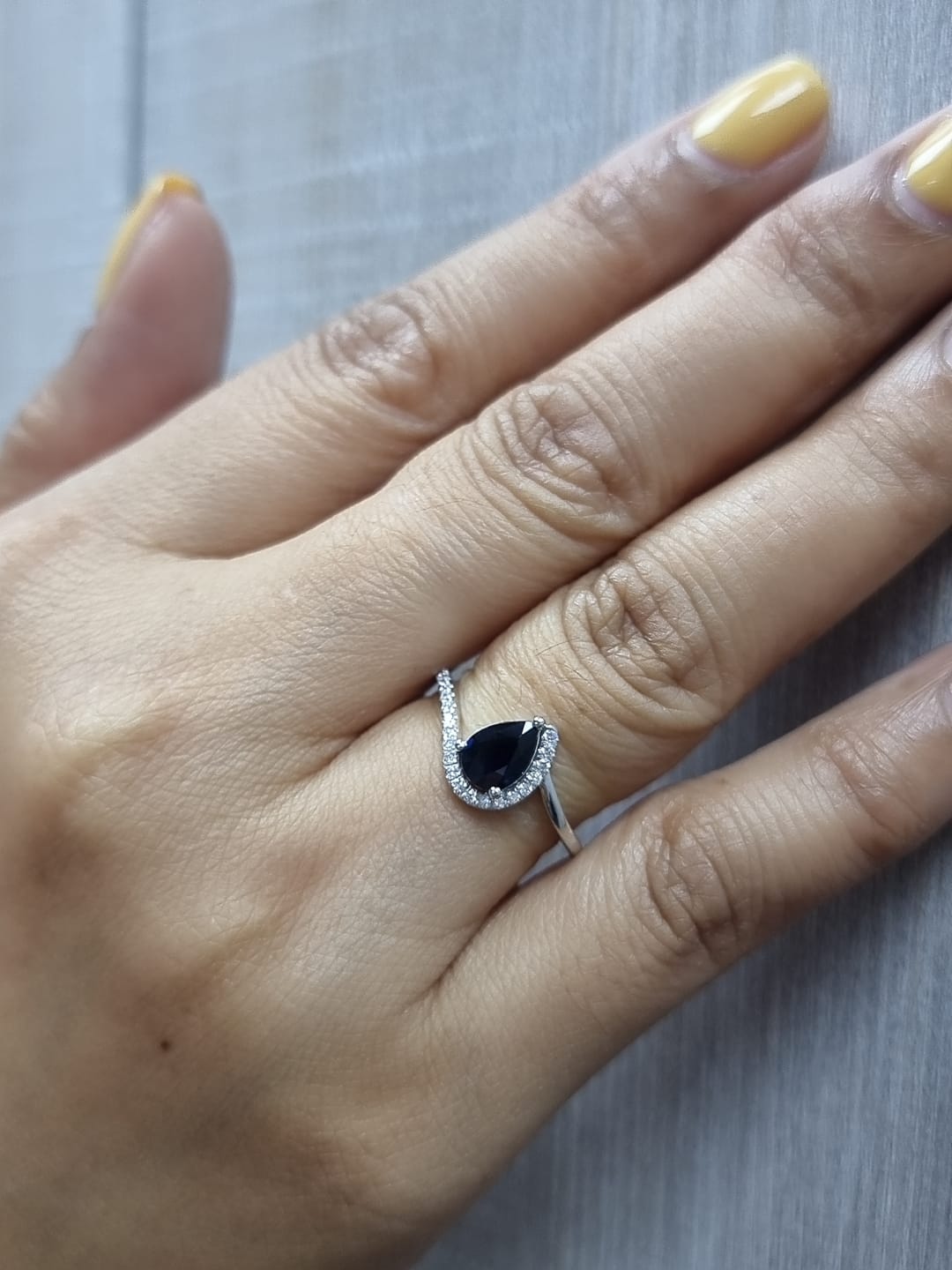 Ring on finger showcasing 0.90 ct blue sapphire, 0.14 ct diamond accents, and elegant bypass design