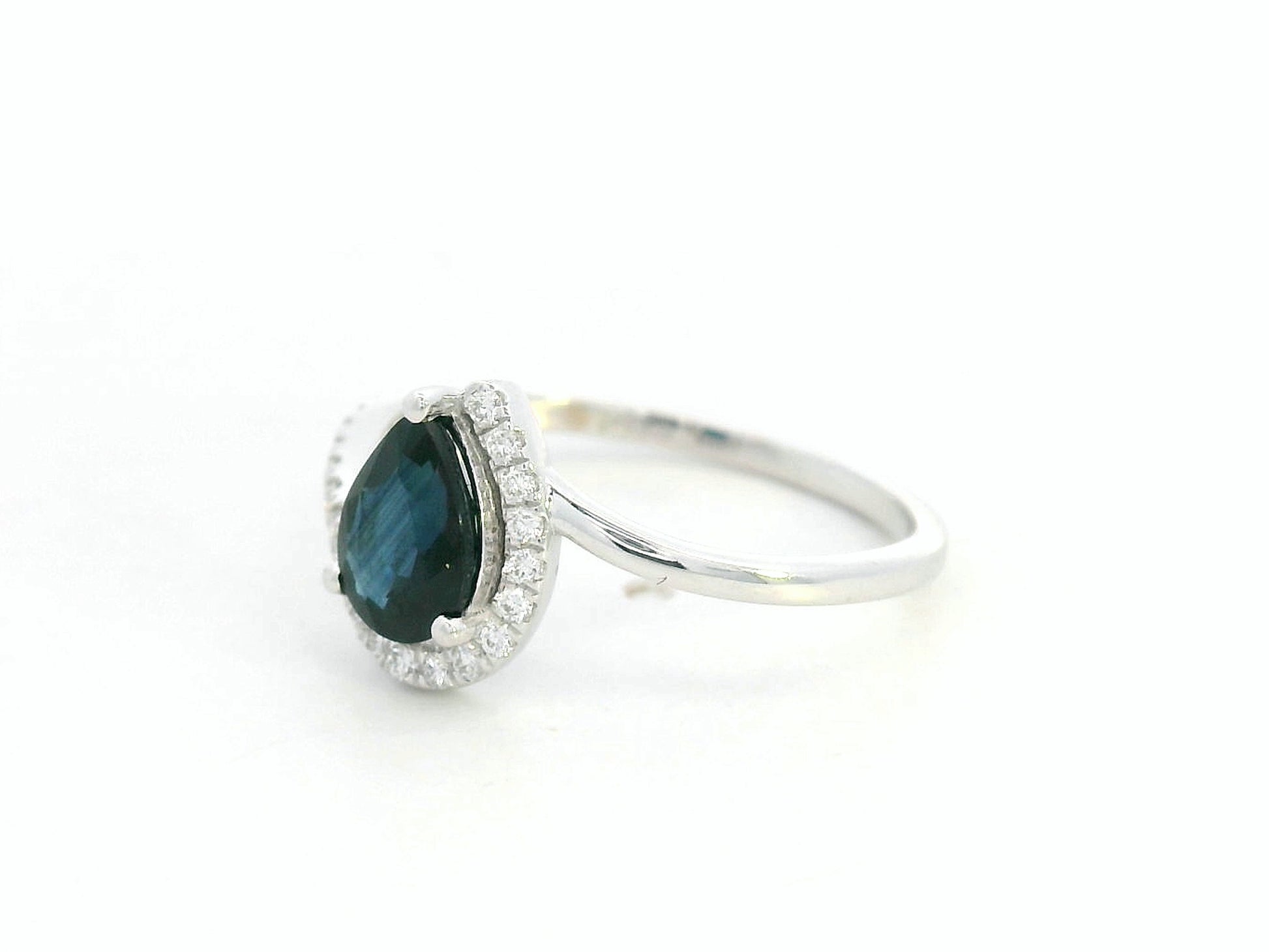 Side view of 18k white gold bypass ring highlighting curved diamond-studded band and pear-shaped blue sapphire