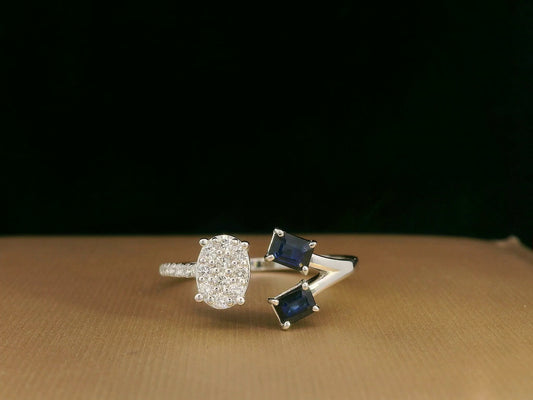 18K white gold open-shank ring featuring an oval diamond cluster on one side and two emerald-cut blue sapphires on the other, accented with pavé diamonds along the band.