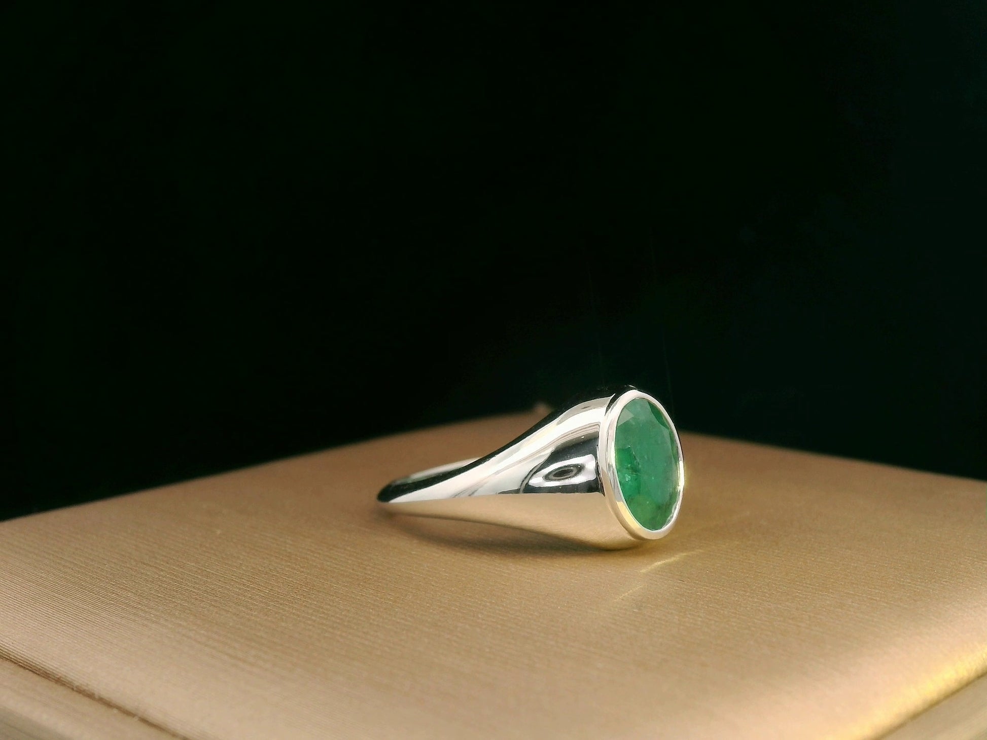 18K white gold men’s signet ring featuring a 1.80ct oval-cut emerald in a sleek bezel setting with a solid tapered band.