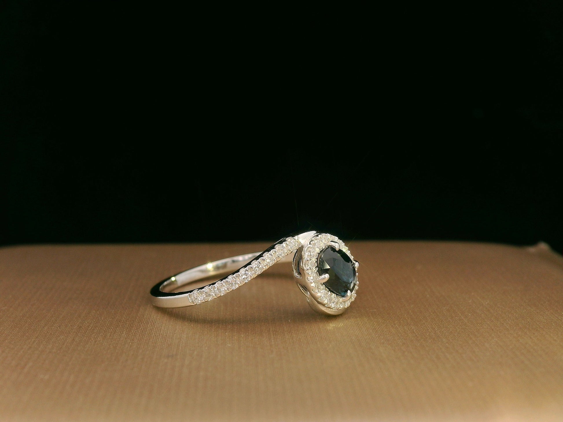 Oval blue sapphire halo ring with pavé diamonds in 18K white gold, bypass design