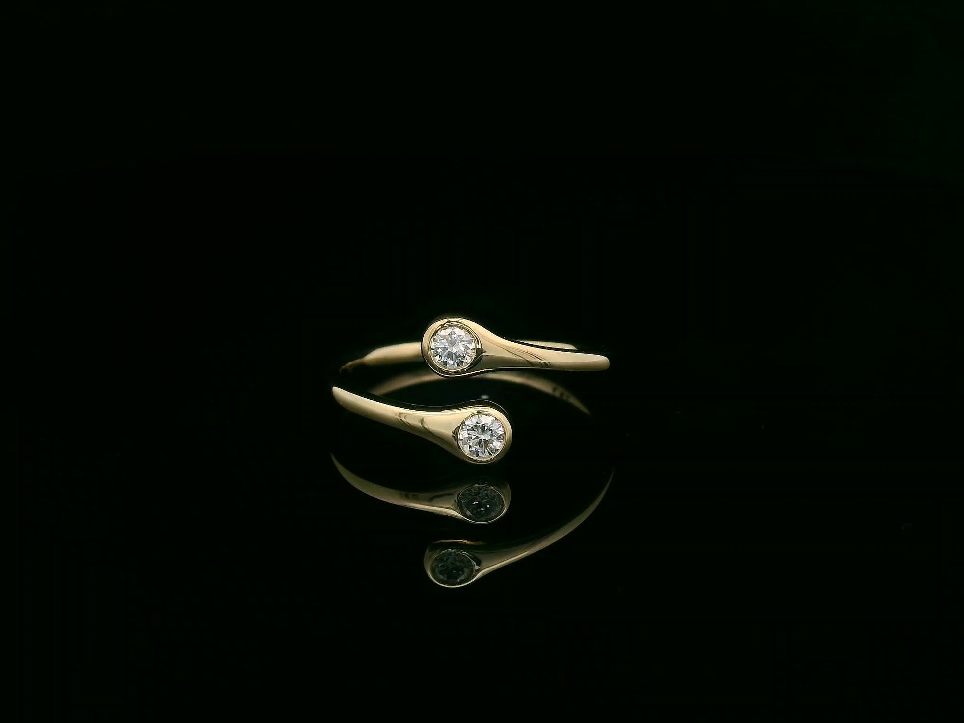 18K yellow gold diamond bypass ring with two round bezel-set diamonds, modern open design by Emirates Diamonds
