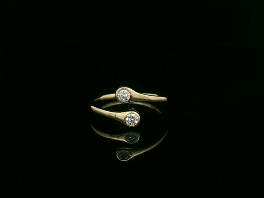 18K yellow gold diamond bypass ring with two round bezel-set diamonds, modern open design by Emirates Diamonds