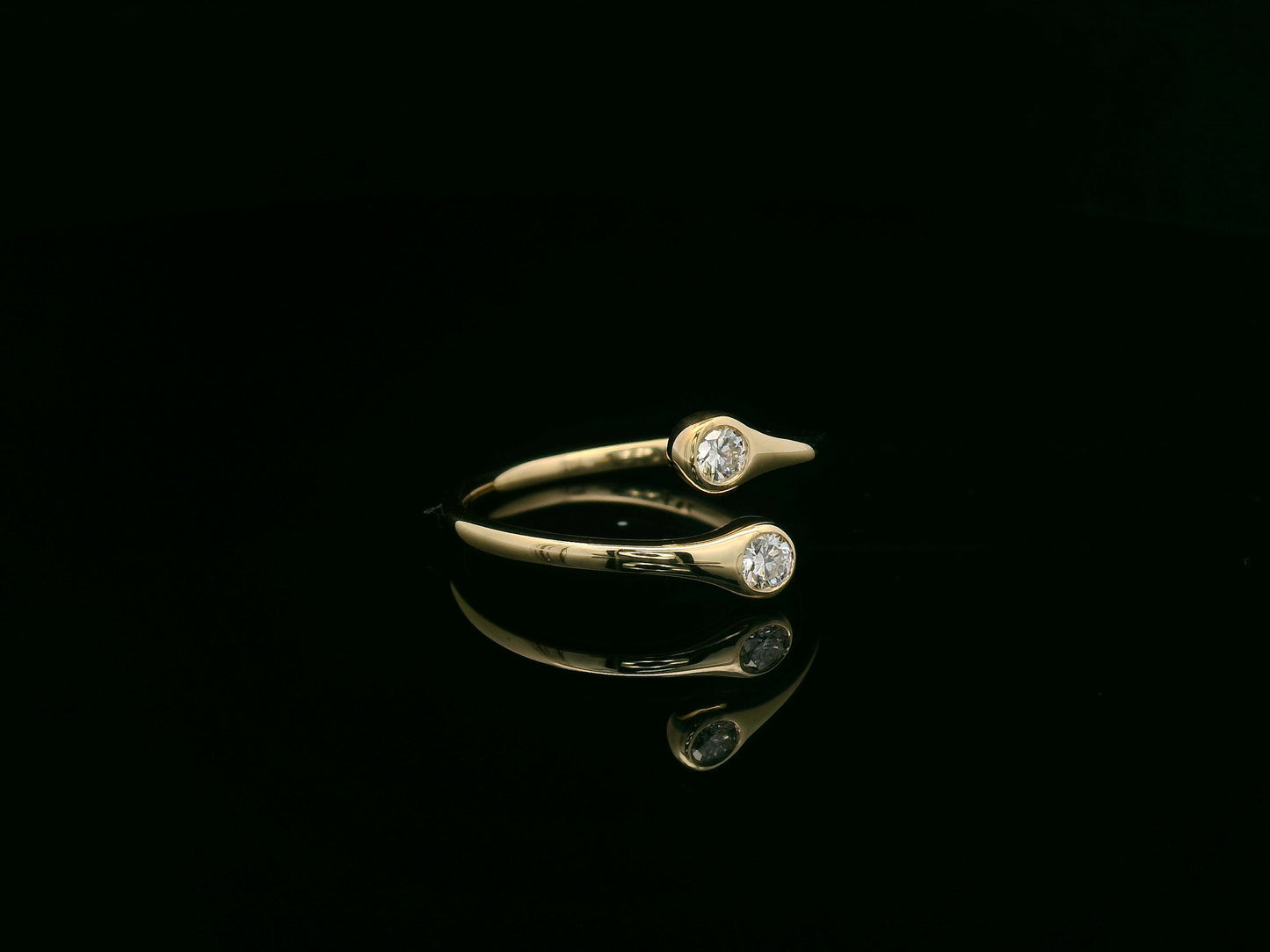 18K yellow gold diamond bypass ring with two round bezel-set diamonds, modern open design by Emirates Diamonds