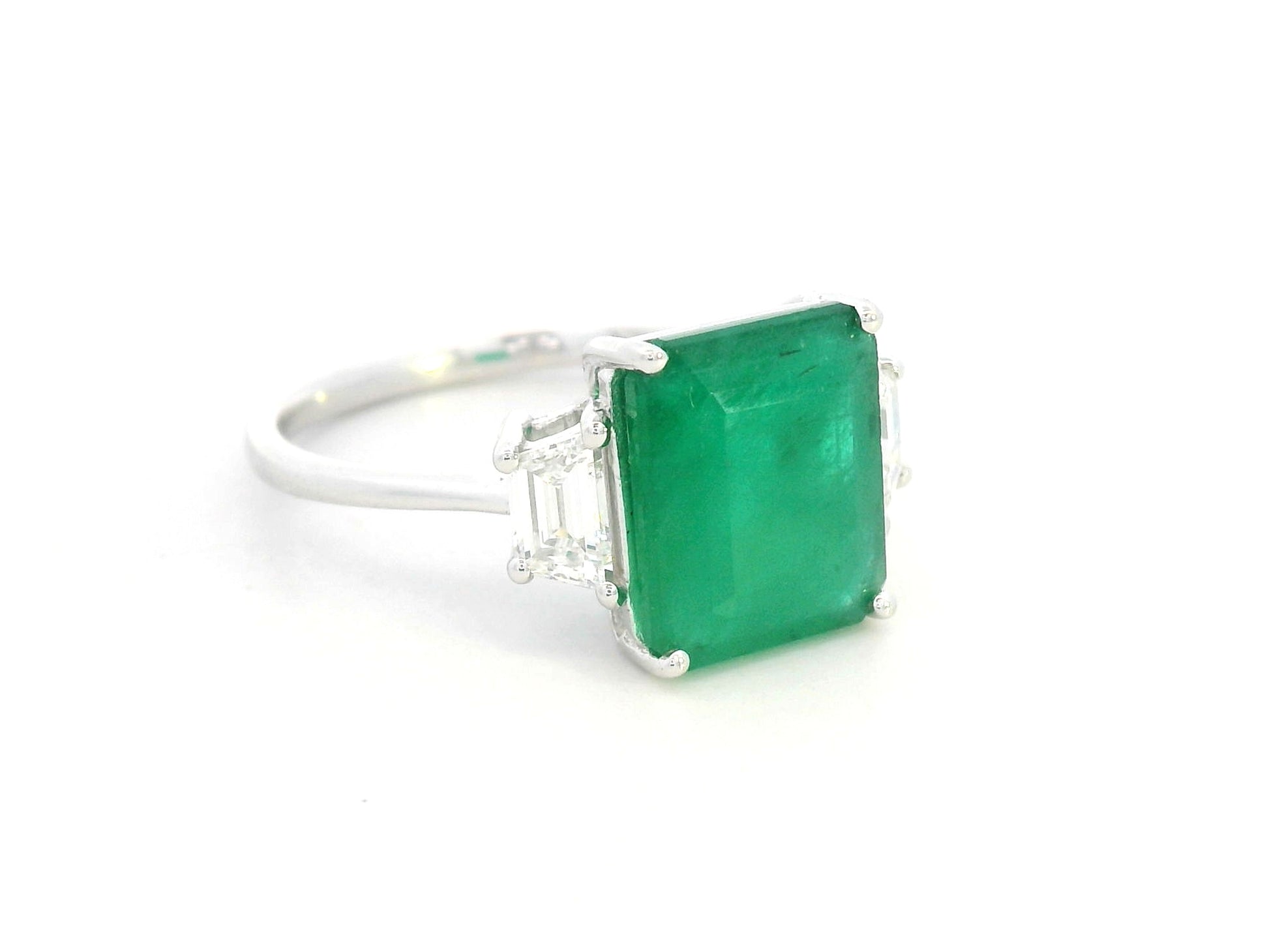 Emerald-cut emerald ring with trapezoid diamond side stones in 18K white gold by Emirates Diamonds.