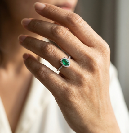 Natural oval emerald ring in 18K white gold featuring a 0.35 carat emerald surrounded by a diamond halo with 0.23 carat total diamond weight.