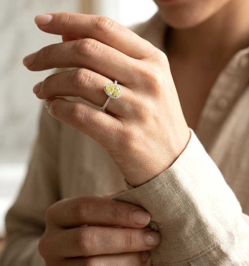 Fancy yellow pear-shaped diamond halo ring in 18K white gold with pavé diamond band and GIA certified center stone.
