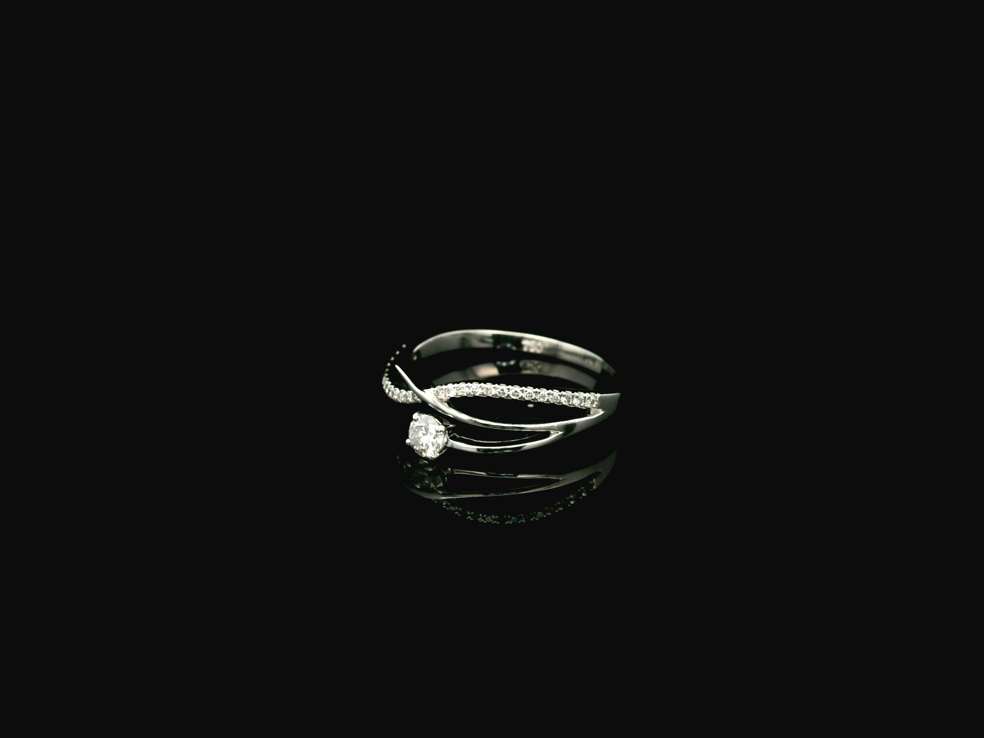 Elegant 18K white gold twist diamond ring featuring a brilliant round centre diamond with flowing pavé diamond crossover band by Emirates Diamonds.