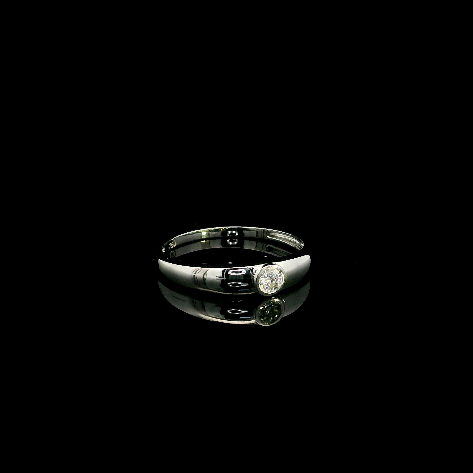 18K white gold bezel set solitaire diamond ring featuring a 0.11 carat natural round brilliant diamond with a smooth polished band.
