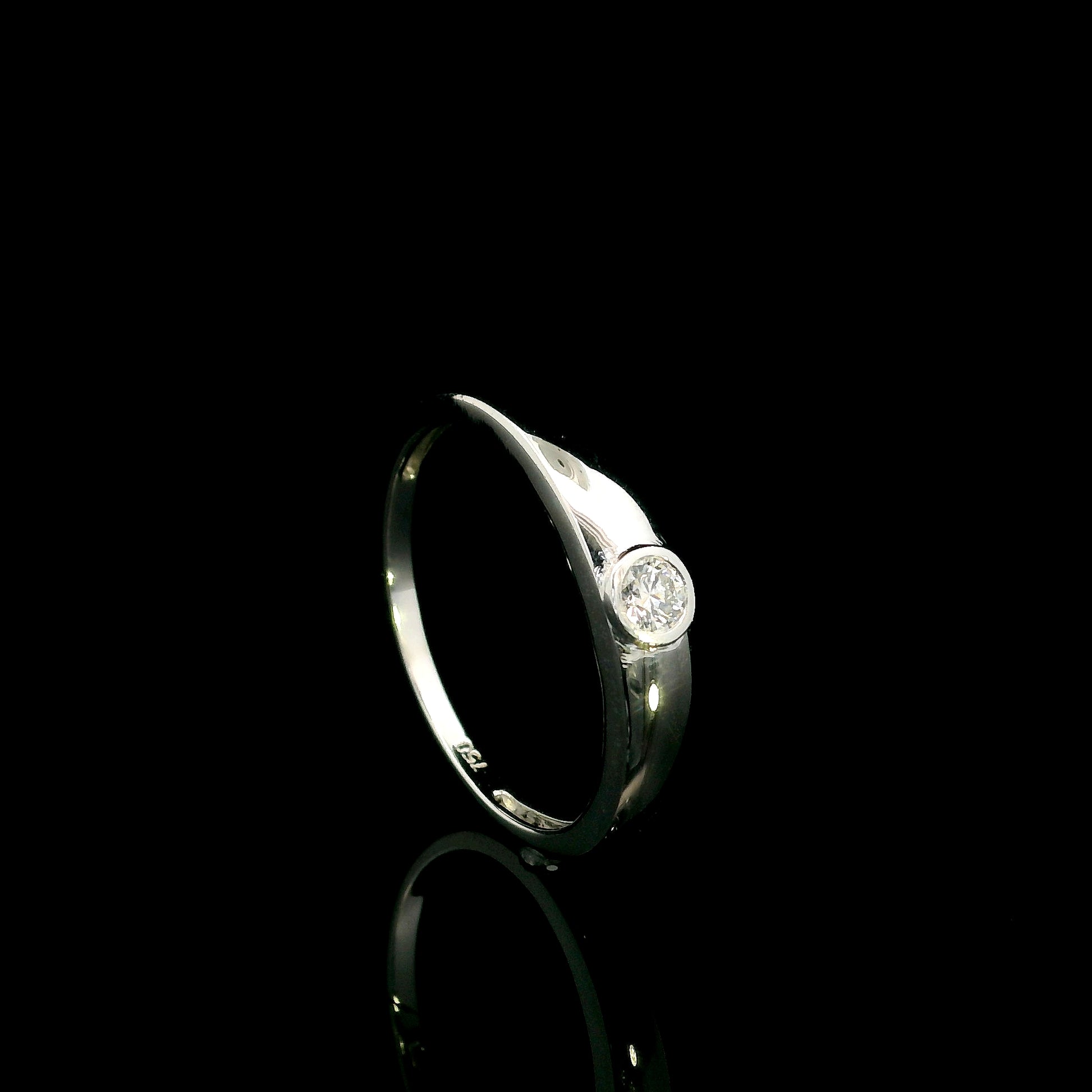 18K white gold bezel set solitaire diamond ring featuring a 0.11 carat natural round brilliant diamond with a smooth polished band.