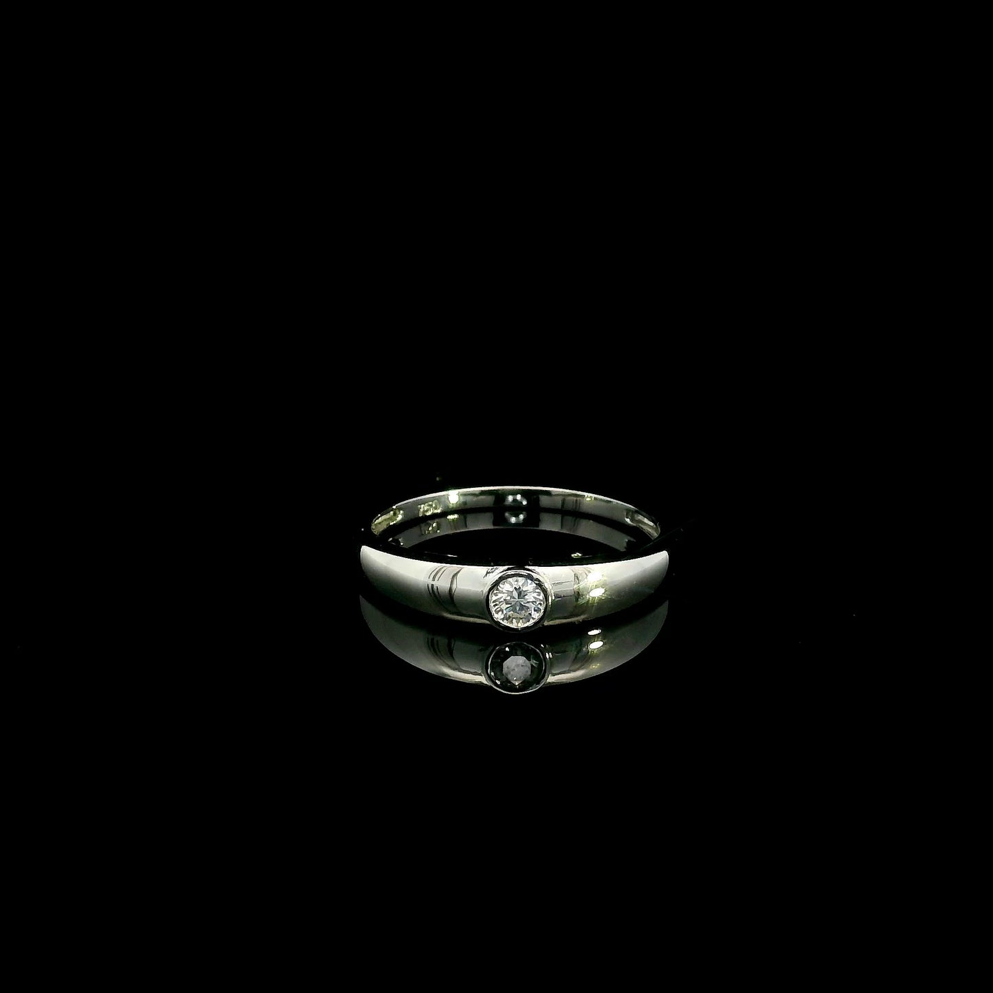 18K white gold bezel set solitaire diamond ring featuring a 0.11 carat natural round brilliant diamond with a smooth polished band.