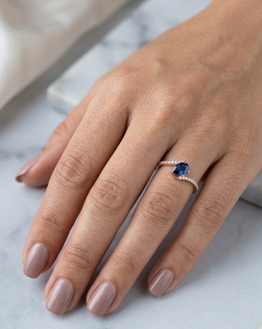 Natural pear-shaped blue sapphire ring in 18K rose gold featuring a 0.78 carat blue sapphire with a bypass diamond band set with 0.19 carat natural diamonds.