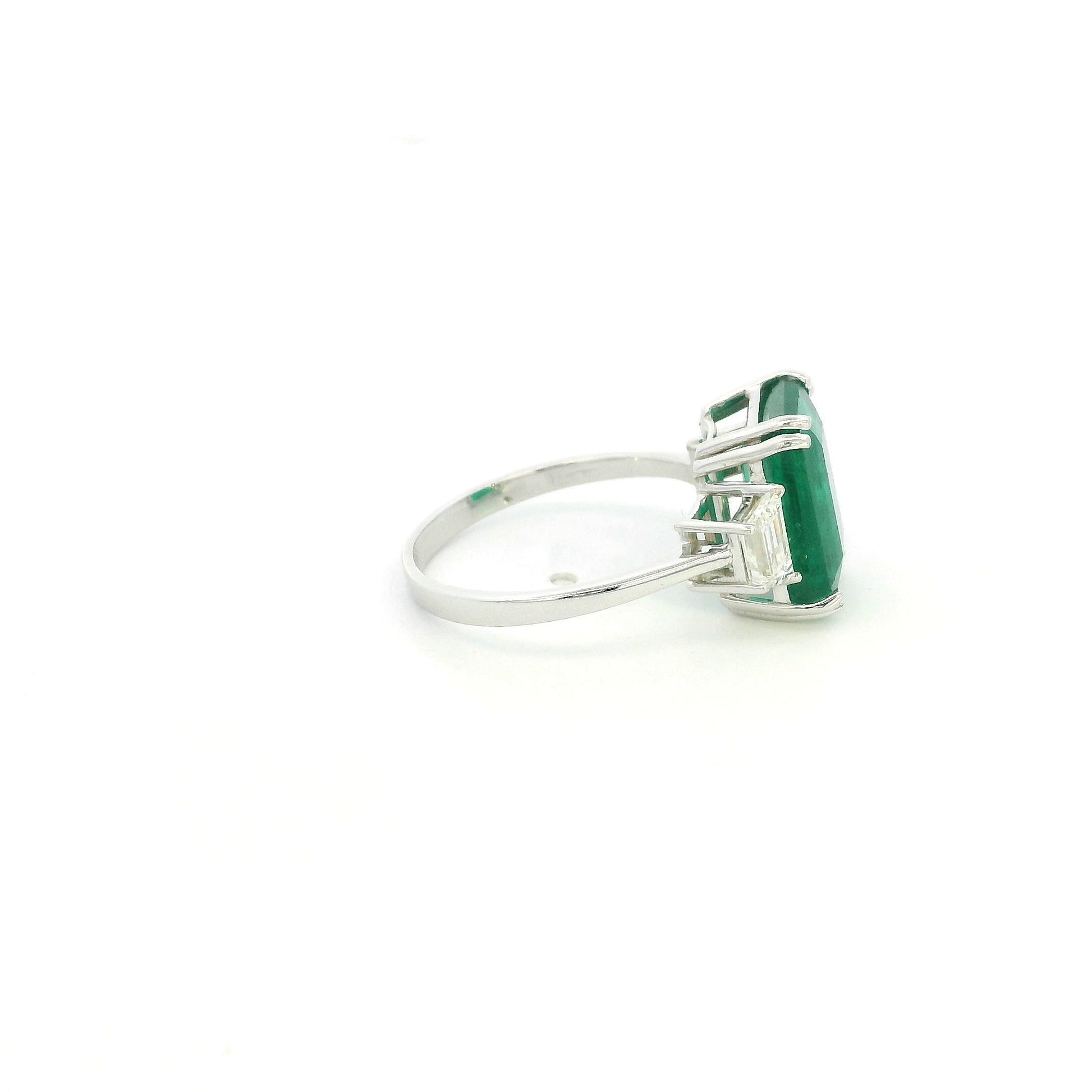 Emerald cut natural emerald and trapezoid diamond three stone ring in 18K white gold featuring a 4.77 carat emerald and 0.75 carat diamonds