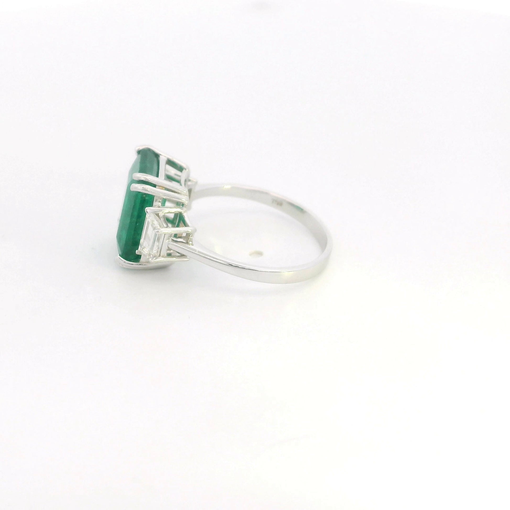 Emerald cut natural emerald and trapezoid diamond three stone ring in 18K white gold featuring a 4.77 carat emerald and 0.75 carat diamonds
