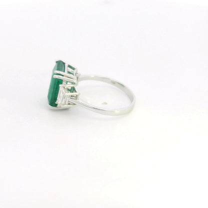 Emerald cut natural emerald and trapezoid diamond three stone ring in 18K white gold featuring a 4.77 carat emerald and 0.75 carat diamonds
