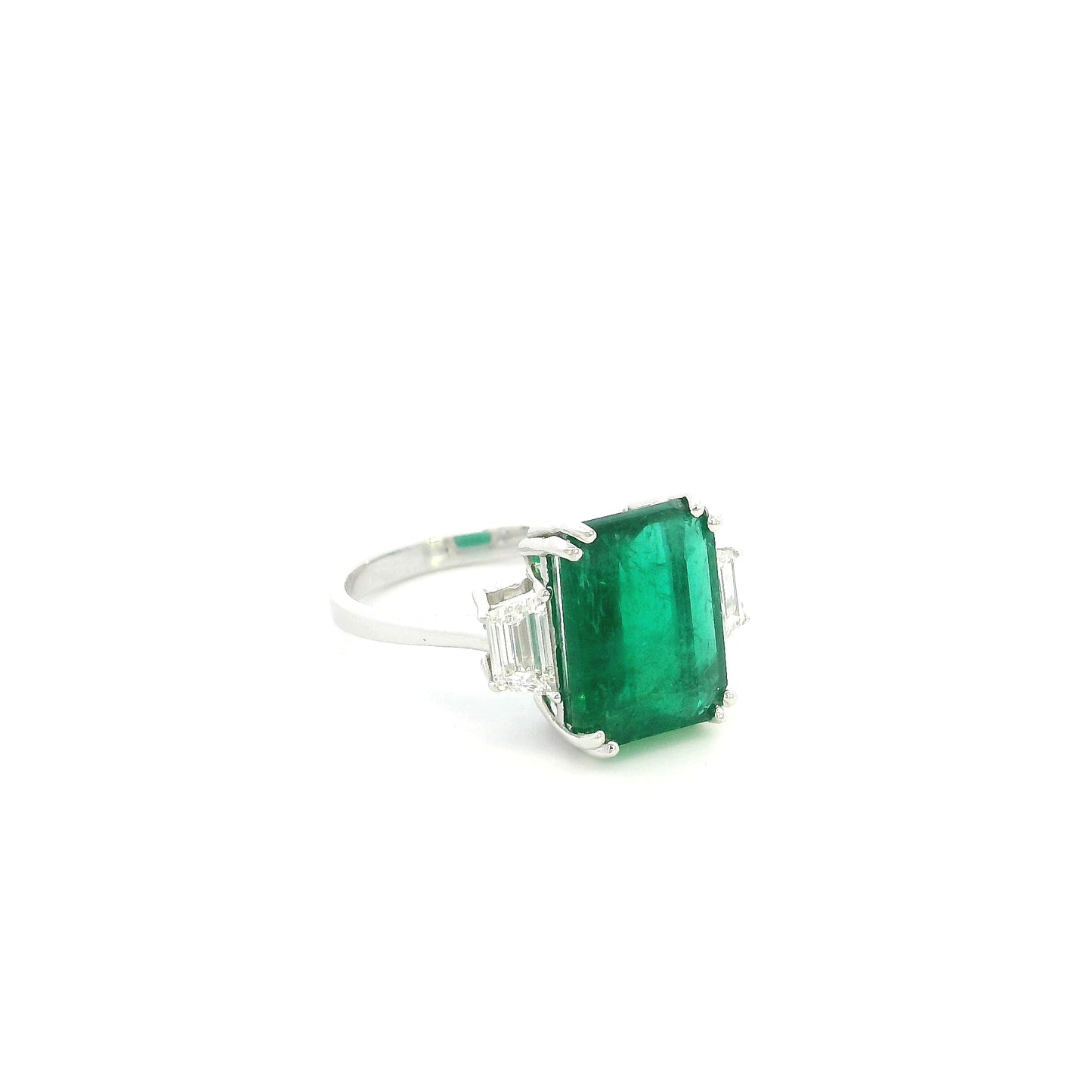 Emerald cut natural emerald and trapezoid diamond three stone ring in 18K white gold featuring a 4.77 carat emerald and 0.75 carat diamonds