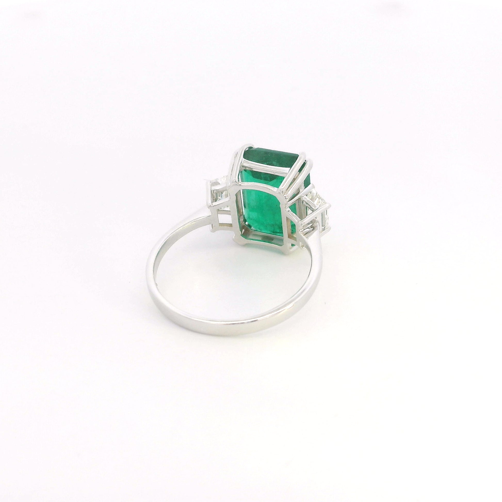 Emerald cut natural emerald and trapezoid diamond three stone ring in 18K white gold featuring a 4.77 carat emerald and 0.75 carat diamonds