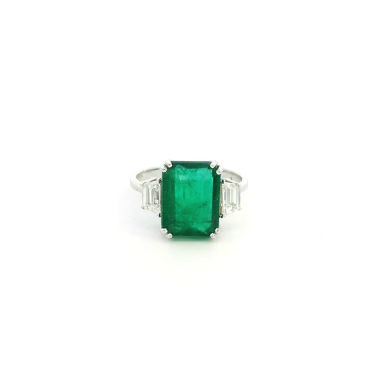 Emerald cut natural emerald and trapezoid diamond three stone ring in 18K white gold featuring a 4.77 carat emerald and 0.75 carat diamonds