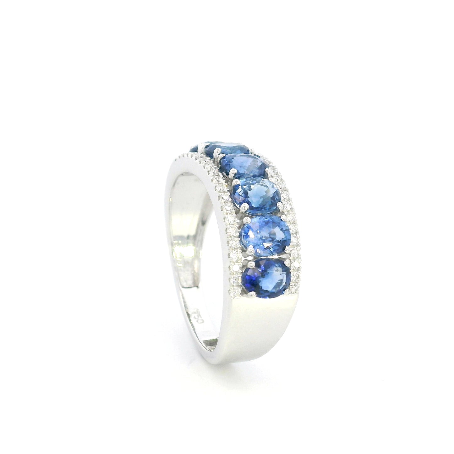 Blue sapphire and diamond band ring in 18K white gold featuring oval blue sapphires framed by rows of round brilliant diamonds.