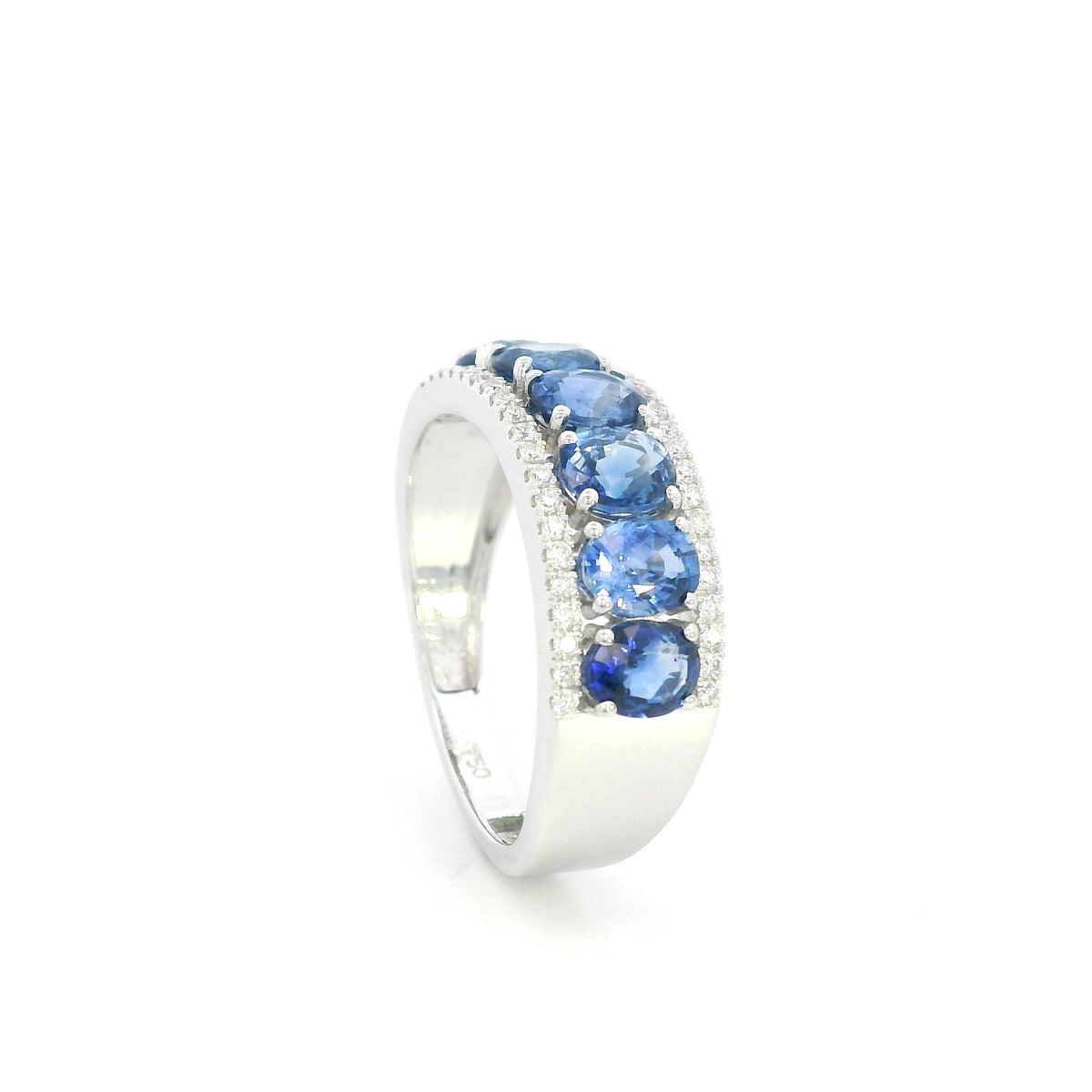 Blue sapphire and diamond band ring in 18K white gold featuring oval blue sapphires framed by rows of round brilliant diamonds.