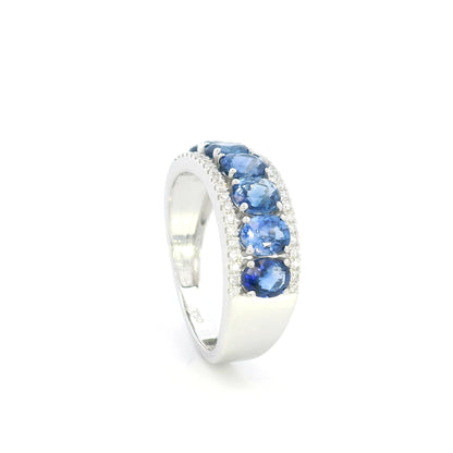 Blue sapphire and diamond band ring in 18K white gold featuring oval blue sapphires framed by rows of round brilliant diamonds.