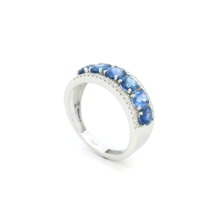 Blue sapphire and diamond band ring in 18K white gold featuring oval blue sapphires framed by rows of round brilliant diamonds.
