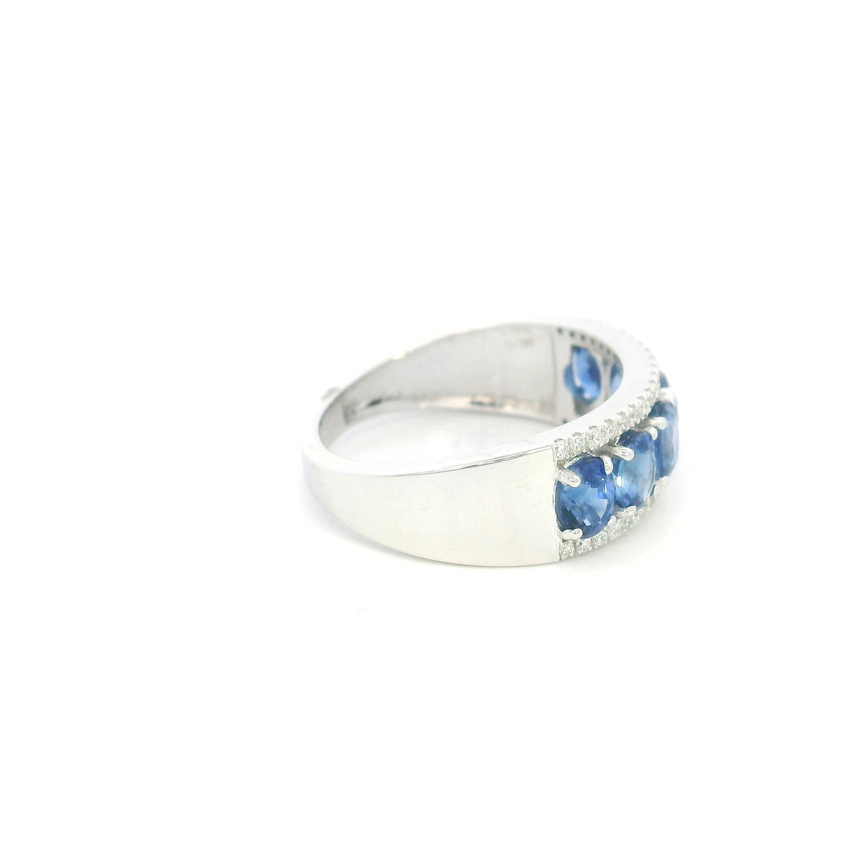 Blue sapphire and diamond band ring in 18K white gold featuring oval blue sapphires framed by two rows of sparkling diamonds, worn on a hand.
