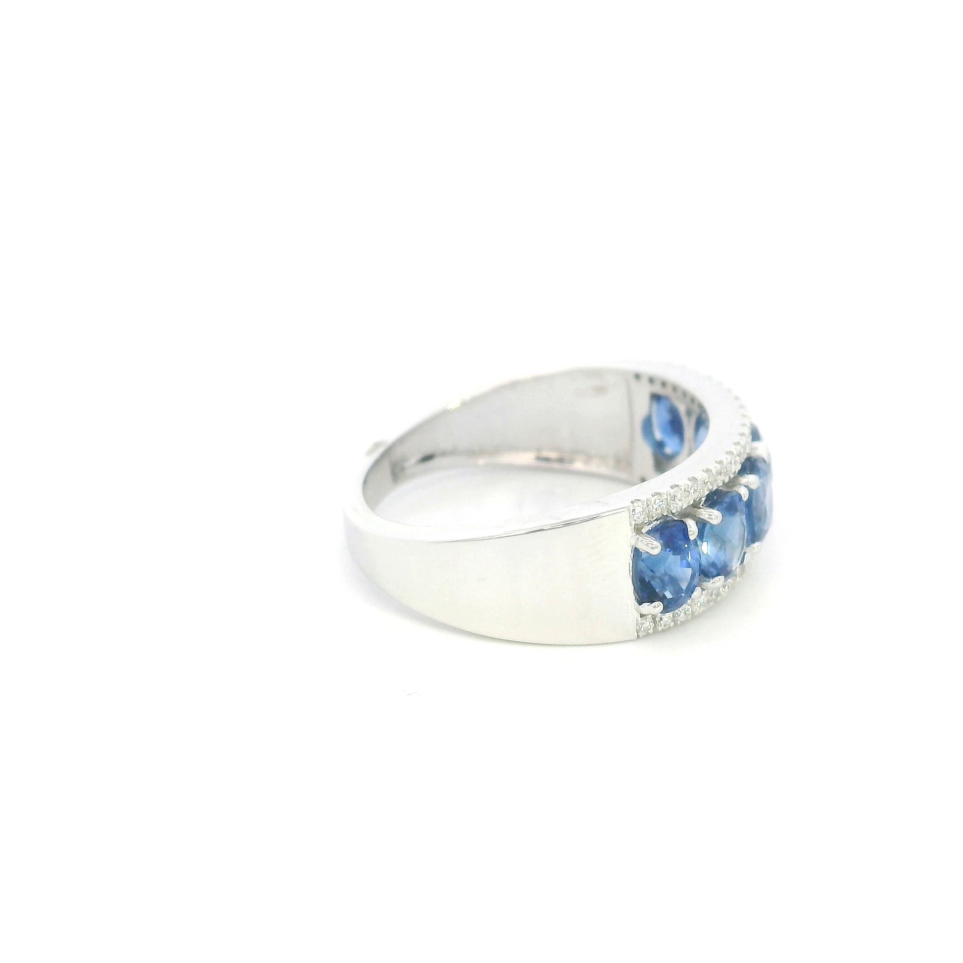Blue sapphire and diamond band ring in 18K white gold featuring oval blue sapphires framed by rows of round brilliant diamonds.