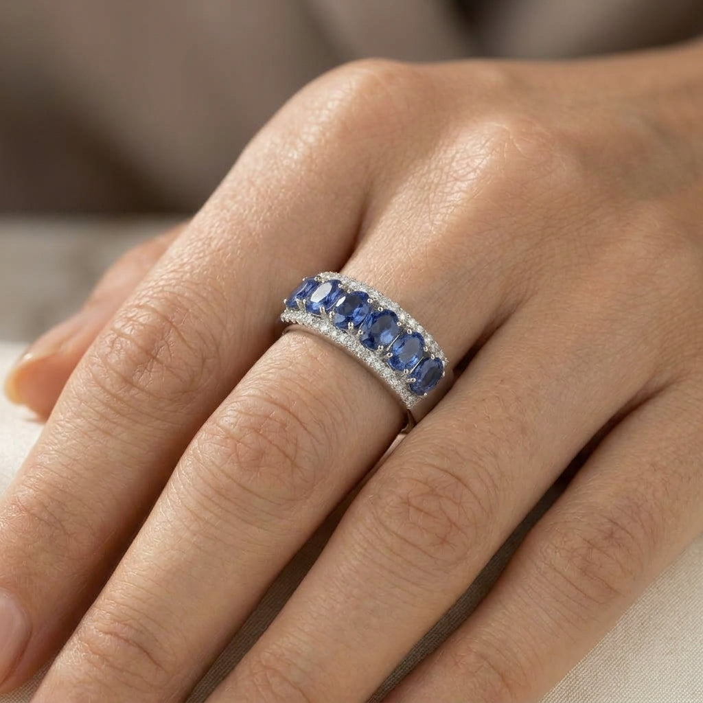 Blue sapphire and diamond band ring in 18K white gold featuring oval blue sapphires framed by two rows of sparkling diamonds, worn on a hand.