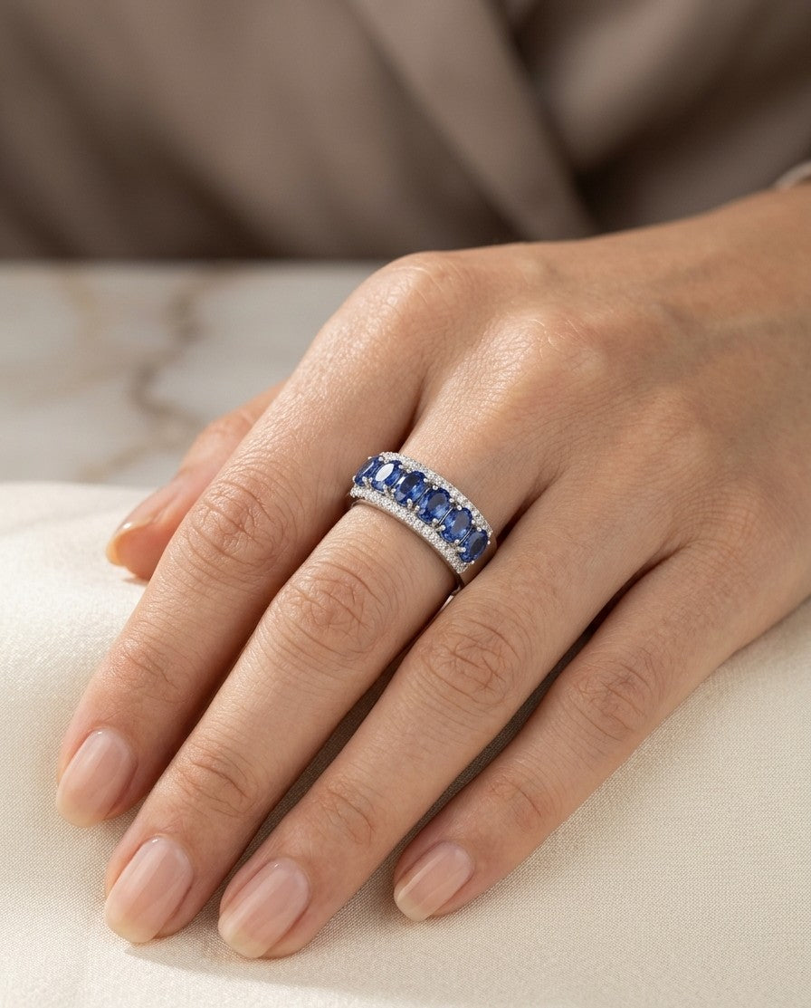 Blue sapphire and diamond band ring in 18K white gold featuring oval blue sapphires framed by rows of round brilliant diamonds.