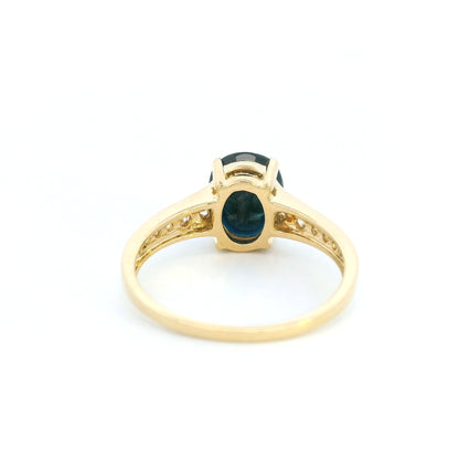 Blue sapphire and diamond ring in 18K yellow gold featuring an oval blue sapphire with round brilliant diamond-set shoulders.