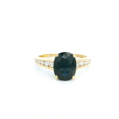 Blue sapphire and diamond ring in 18K yellow gold featuring an oval blue sapphire with round brilliant diamond-set shoulders.
