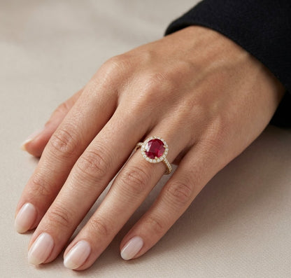 Ruby and diamond halo ring in 18K yellow gold featuring a round red ruby surrounded by diamonds with diamond-set shoulders.