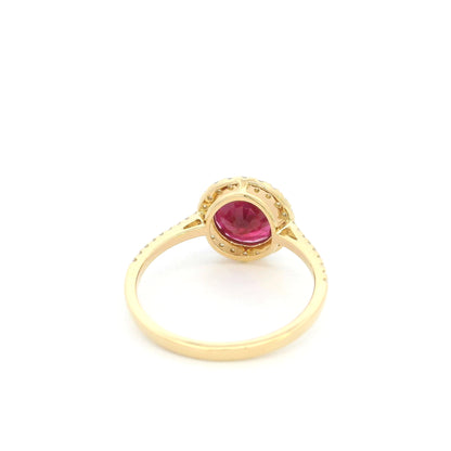 Ruby and diamond halo ring in 18K yellow gold featuring a round red ruby surrounded by diamonds with diamond-set shoulders.