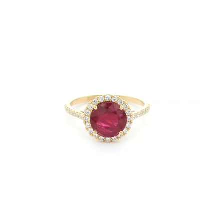 Ruby and diamond halo ring in 18K yellow gold featuring a round red ruby surrounded by diamonds with diamond-set shoulders.
