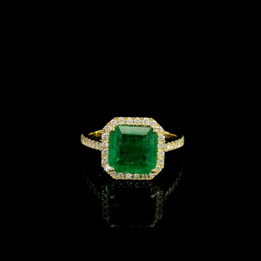 Emerald and diamond halo ring in 18K yellow gold with a rectangular green emerald, diamond surround and diamond-set shoulders.