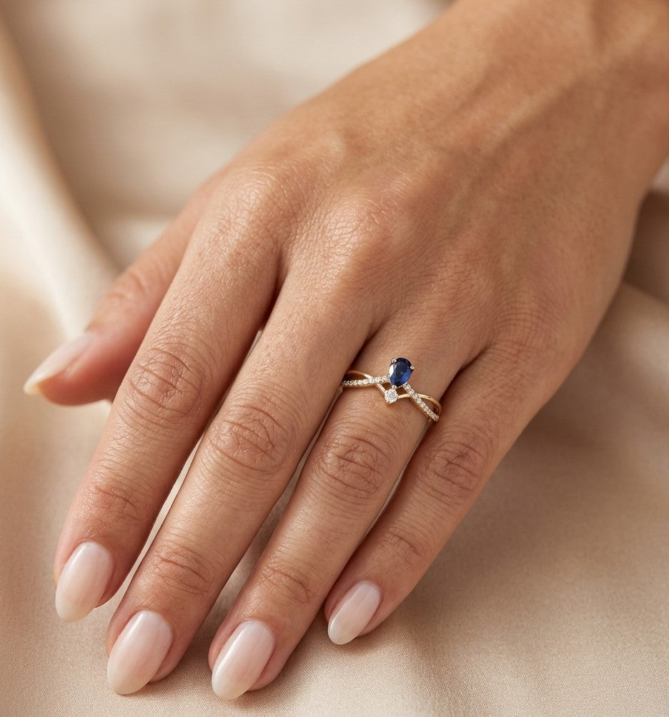 Pear shaped blue sapphire and diamond ring in 18K yellow gold with sweeping diamond-set design.