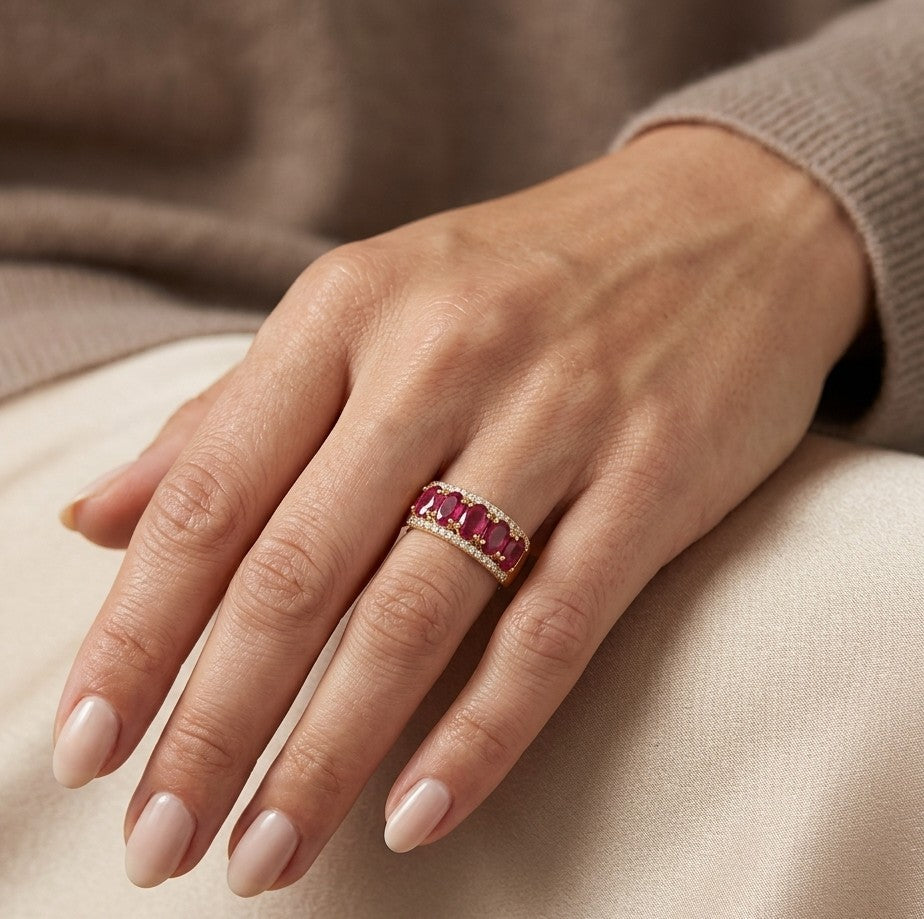 Oval ruby and diamond band ring in 18K yellow gold with a row of rubies framed by round diamonds.