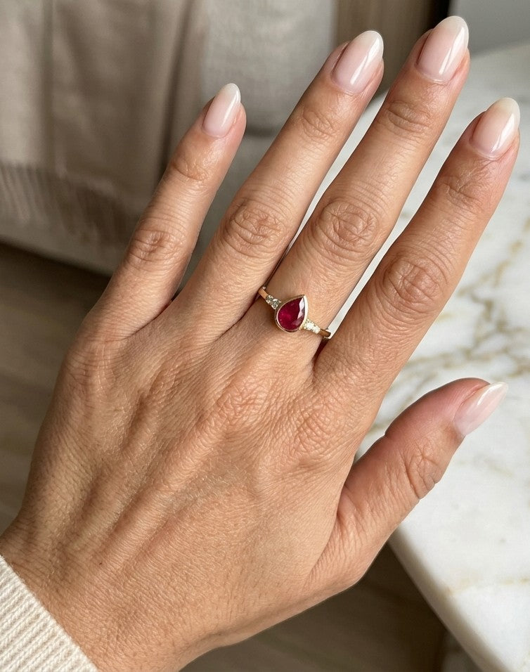 Pear-shaped red ruby ring in 18K yellow gold with a smooth bezel setting and small round diamonds along both shoulders.