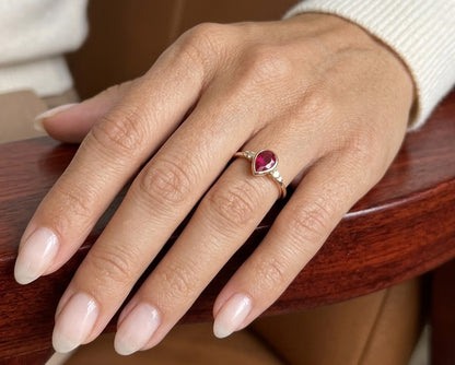 Pear-shaped red ruby ring in 18K yellow gold with a smooth bezel setting and small round diamonds along both shoulders.