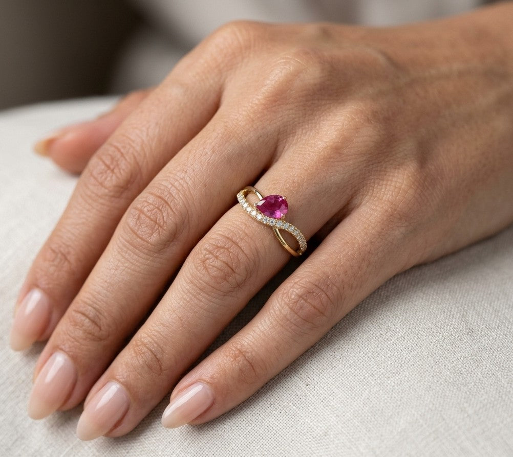 Pear shaped ruby and diamond ring in 18K yellow gold featuring a sweeping diamond-set curved band and asymmetrical design.