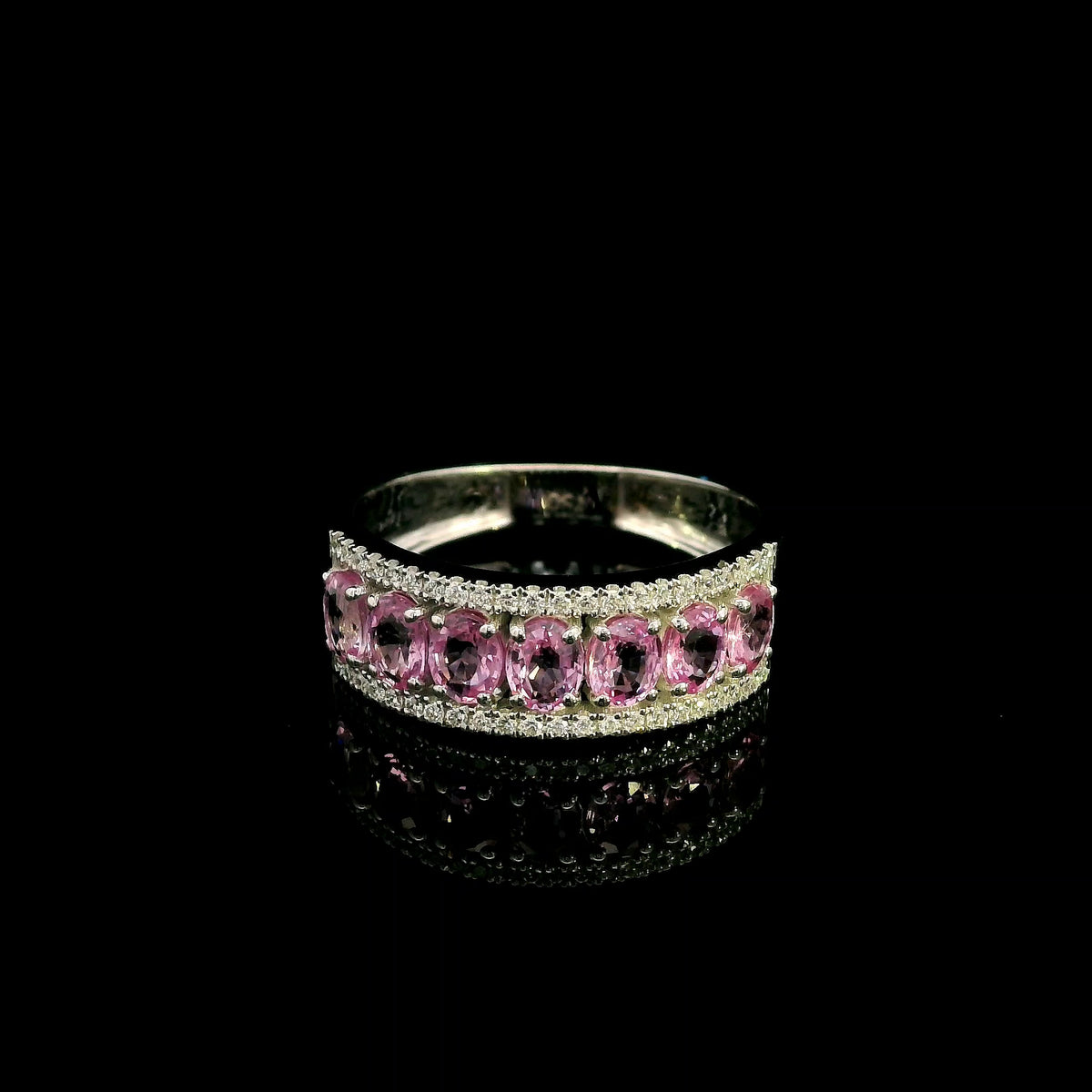 Pink sapphire and diamond band ring in 18K white gold featuring oval pink sapphires framed by two rows of sparkling diamonds.
