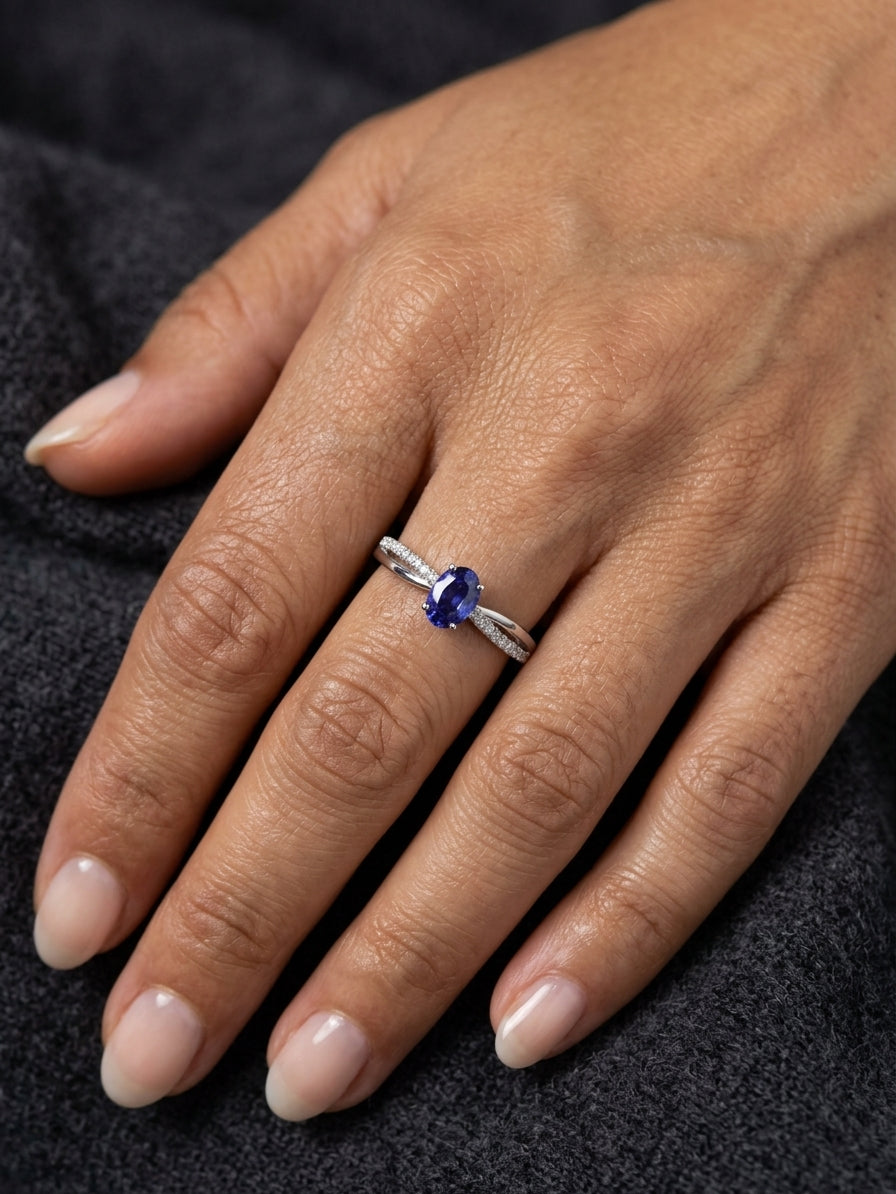 Oval blue sapphire ring with diamond-set shoulders in polished 18K white gold, featuring a four-prong centre gemstone setting.