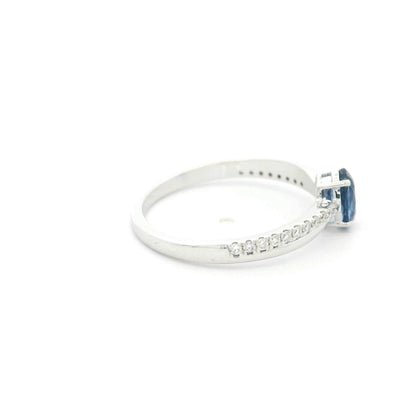 Oval blue sapphire ring with diamond-set shoulders in polished 18K white gold, featuring a four-prong centre gemstone setting.