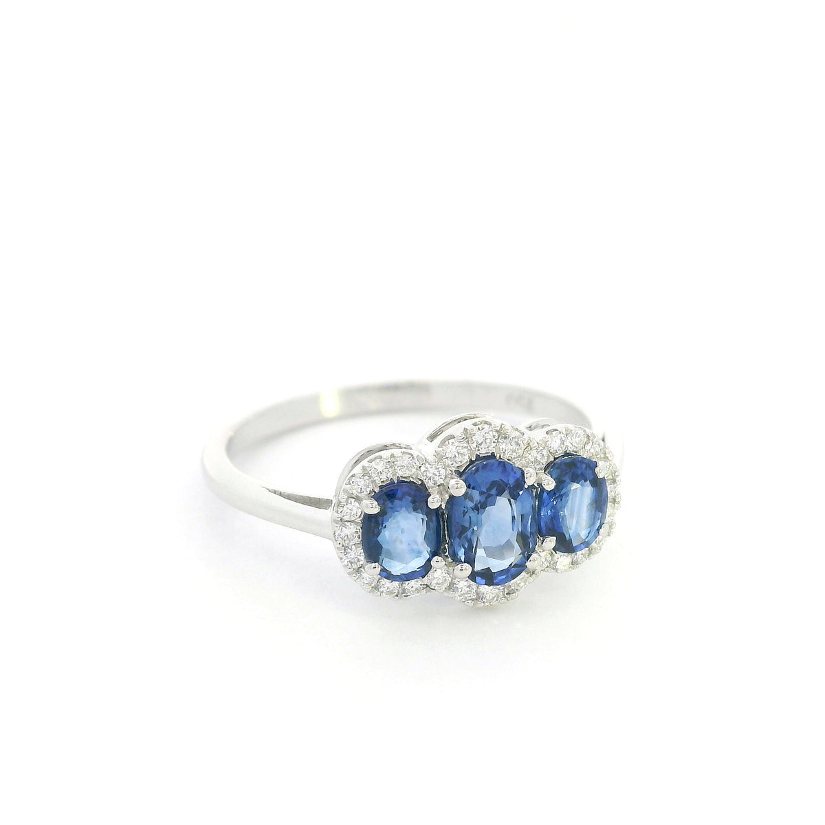 Three stone blue sapphire ring in 18K white gold featuring oval sapphires surrounded by individual diamond halos.
