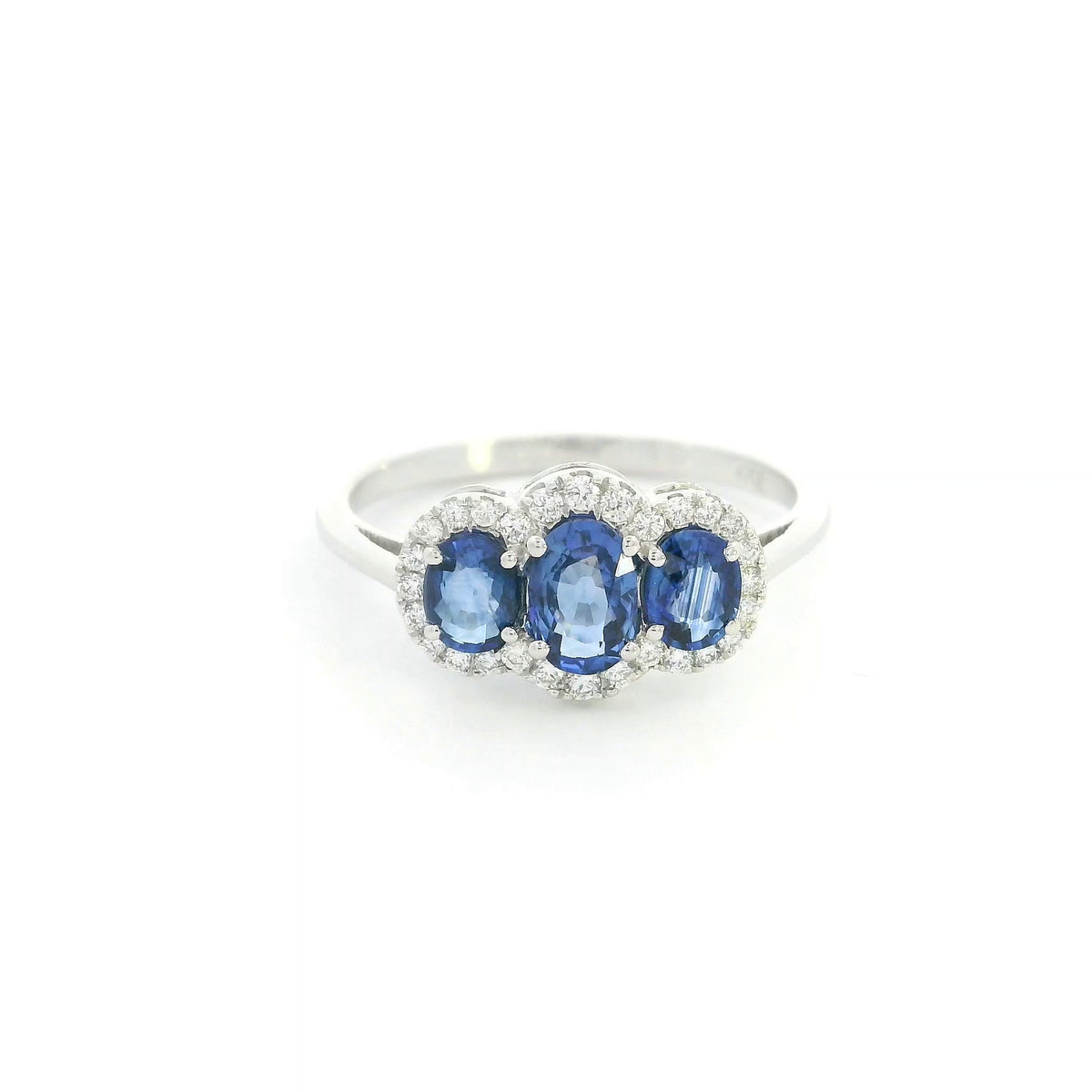 Three stone blue sapphire ring in 18K white gold featuring oval sapphires surrounded by individual diamond halos.