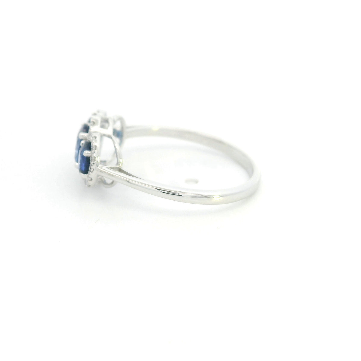 Three stone blue sapphire ring in 18K white gold featuring oval sapphires surrounded by individual diamond halos.