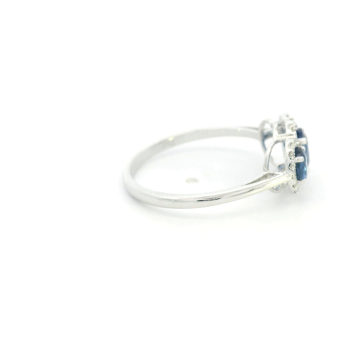 Three stone blue sapphire ring in 18K white gold featuring oval sapphires surrounded by individual diamond halos.