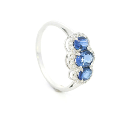Three stone blue sapphire ring in 18K white gold featuring oval sapphires surrounded by individual diamond halos.